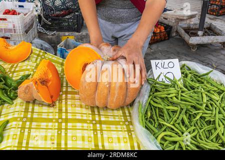 Couper la grosse citrouille jaune pour être vendue en petits morceaux à un étal de marché. Banque D'Images