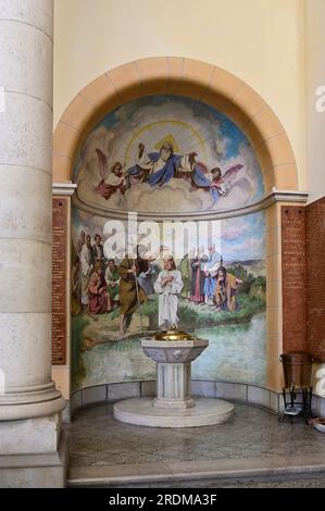 Vienne, Autriche. 19 juillet 2023. Église paroissiale de St. François d'Assise. Les fonts baptismaux devant l'image du baptême de Jésus Banque D'Images