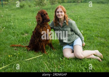 Red Irish Setter processus de formation en extérieur. Belle blonde souriante bonne jeune femme en short denim sont assis au verre et l'entraînement d'un mignon samoyed Banque D'Images