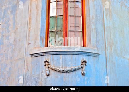 Détail d'architecture abstraite : une belle fenêtre d'angle avec cadre en bois doré chaud et guirlande de plâtre ornementale ci-dessous, entourée de bleu pastel Banque D'Images