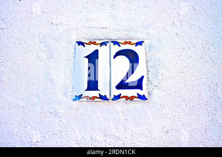 Simple numéro 12, douze, carreaux floraux simples sur un mur blanc avec un léger moulage bleu. Banque D'Images