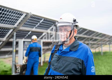 Ingénieur de maintenance mature debout devant les panneaux solaires. Technicien maintenance des cellules solaires sur la centrale d'énergie solaire sous la lumière du soleil du matin Banque D'Images