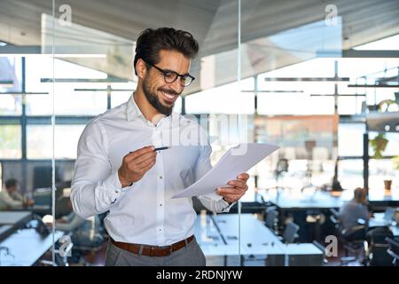 Heureux jeune homme d'affaires latin vérifiant les documents financiers dans le bureau. Banque D'Images