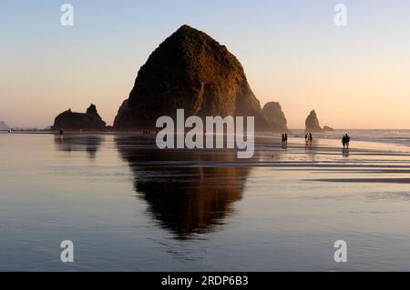 Les gens se promènent sur la plage au coucher du soleil à Haystack Rock et Tidepools à Cannon Beach, Oregon, USA Banque D'Images