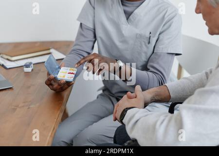 Gros plan d'une infirmière méconnaissable expliquant l'horaire de la médecine à un homme âgé en maison de retraite Banque D'Images