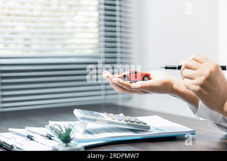 Femme avec document d'assurance automobile ou papier de location. Signature écrite sur le contrat ou l'accord. Acheter ou vendre un véhicule neuf ou d'occasion. Clés de voiture sur la table Banque D'Images