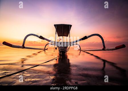 Bali Sanur, bateau de pêche traditionnel au lever du soleil. Gros plan dans l'eau peu profonde et calme avec rétro-éclairage et grand ciel. jukung Banque D'Images