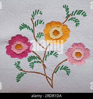 Bouquet de broderie de fleurs rouges, jaunes et roses et feuilles sur fond blanc. Banque D'Images