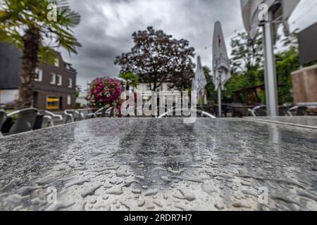 Duisburg, Allemagne. 23 juillet 2023. Gouttes de pluie sur la table d'un restaurant à Duisburg, les parasols fermés, nuages sombres dans le ciel. Les habitants de Rhénanie-du-Nord-Westphalie doivent se préparer aux jours de pluie. Crédit : Christoph Reichwein/dpa/Alamy Live News Banque D'Images