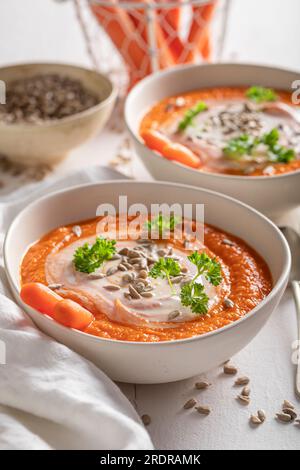 Savoureuse soupe de carottes comme apéritif de printemps et frais. Soupe de carottes avec des herbes et des graines dans un bol blanc. Banque D'Images