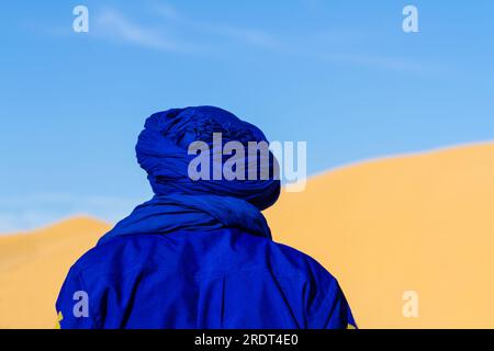 Gros plan. Contexte. Berbère en vêtements traditionnels bleus sur fond d'une grande dune. Vue de derrière. Tunisie, Afrique Banque D'Images
