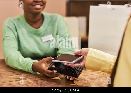 Gros plan de jeune femme méconnaissable payant via la technologie NFC du téléphone en magasin, espace de copie Banque D'Images