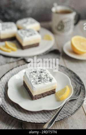 Barres crémeuses au citron et aux graines de pavot sur une assiette blanche décorée de tranches de citron frais. Fond gris et serviette dépouillée. Tasse de café. Banque D'Images