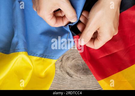 Les mains des femmes cousent le drapeau de l'Allemagne avec le drapeau de l'Ukraine sur le tableau à la maison, la production et le travail, l'Union de deux États, l'amitié Banque D'Images