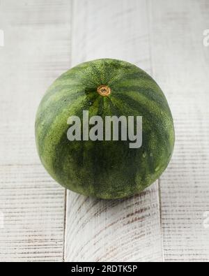 Une petite pastèque mûre entière sur un fond en bois blanc. Fruits et baies. Banque D'Images