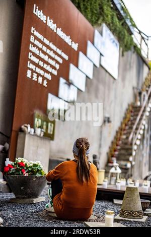 Duisburg, Allemagne. 23 juillet 2023. Une jeune femme est assise par terre au mémorial pour les victimes de la catastrophe de Love Parade. Le 24 juillet 2010, 21 personnes âgées de 17 à 38 ans sont écrasées à la seule entrée et sortie de la technoparade. Au moins 652 visiteurs de Love Parade ont été blessés à ce moment-là. Chaque année, les proches survivants commémorent les victimes. Crédit : Christoph Reichwein/dpa/Alamy Live News Banque D'Images