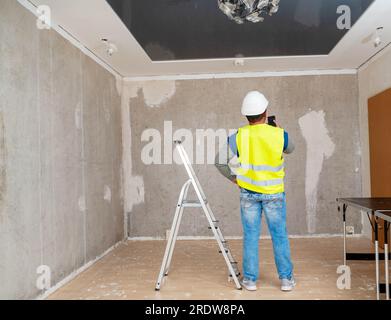 Un maître finisseur dans un casque de sécurité regarde le volume de la rénovation de l'appartement. Constructeur au travail. Banque D'Images