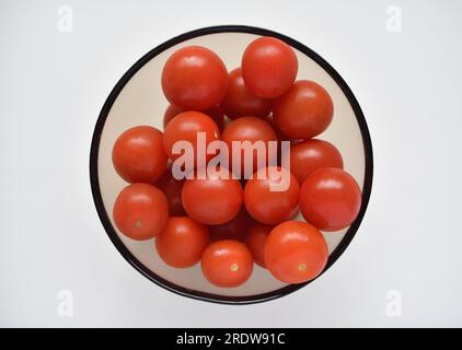 Fruits rouges de petites tomates dans une assiette de verre. Tomates cerises juteuses. Banque D'Images