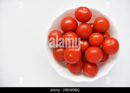 Fruits rouges de petites tomates dans une assiette de verre. Tomates cerises juteuses. Banque D'Images