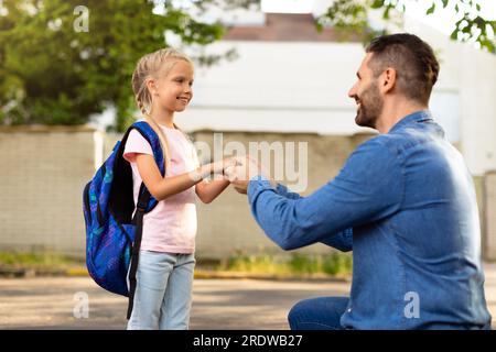 Naviguer dans de nouveaux départs. Père menant sa fille en première année, se tenant la main et parlant avec l'enfant dans la cour arrière Banque D'Images