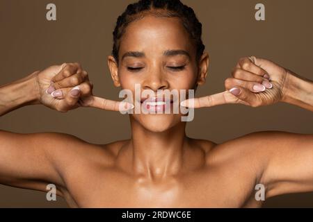 Sourire féminin sain. Femme noire d'âge moyen souriant, pointant vers ses dents blanches parfaites sur fond de studio brun Banque D'Images
