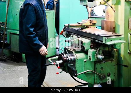 Un travailleur masculin travaille sur un plus grand tour de serrurier de fer métallique, de l'équipement pour les réparations, des travaux de métal dans un atelier dans une usine métallurgique dans un produ de réparation Banque D'Images