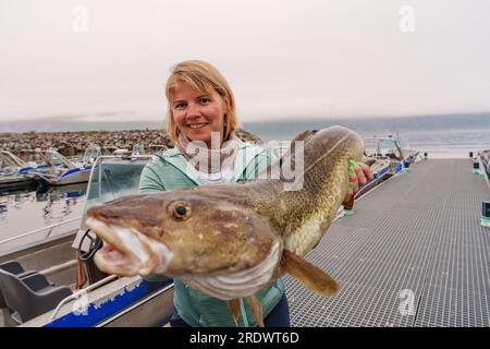 Heureuse pêcheuse tenant une grosse morue arctique. Norvège pêche heureuse. Femme avec du poisson de morue dans les mains Banque D'Images