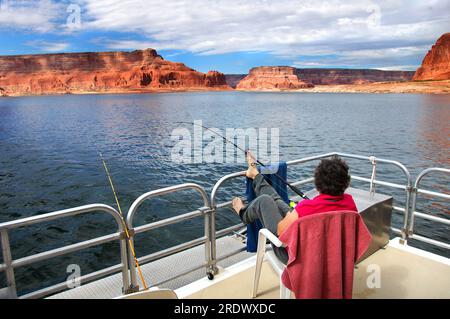 Woman relaxes and enjoys the fantastic views of sandstone cliffs and blue skies.  She is on a houseboat on Lake Powell in Arizona.  She fishes holding Stock Photo