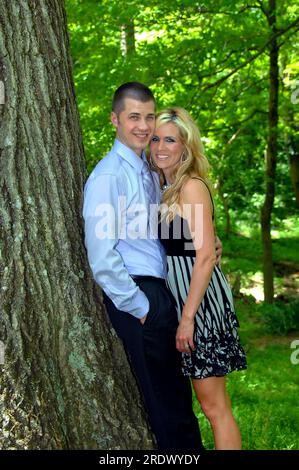 Les jeunes couples se penchent contre un tronc d'arbre et se rapprochent les uns des autres. Ils sourient et regardent la caméra. Les deux portent des vêtements habillés. Banque D'Images