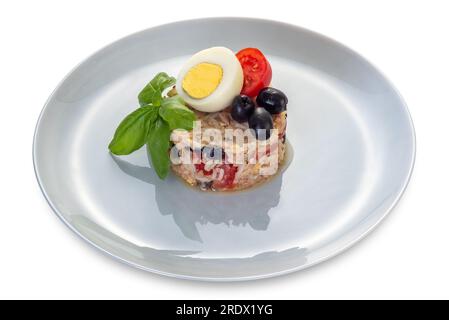 Salade de riz avec thon, tomates, olives et œuf dur et feuilles de basilic dans une assiette couleur perle isolée sur blanc avec chemin de coupe Banque D'Images