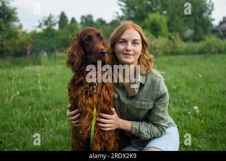 Red Irish Setter processus de formation en extérieur. Belle blonde souriante bonne jeune femme en short denim sont assis au verre et l'entraînement d'un mignon samoyed Banque D'Images