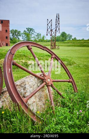 Roue en métal rouillé a rayé contre bloc de béton texturé dans le champ avec de minuscules fleurs et une tour éloignée Banque D'Images