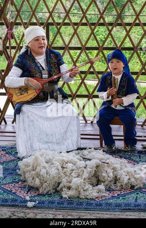 Kazakhstan, village ethno de Huns. Femme kazakhe d'âge moyen jouant la Dombra. Laine sur le sol. Banque D'Images