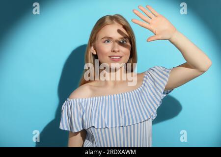 Belle jeune femme s'ombrant avec la main de la lumière du soleil sur fond bleu clair Banque D'Images