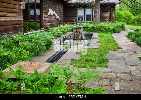 Chemin de pierre autour de la cabane en bois moderne avec des fougères poussant le long de la fontaine d'eau fantaisie avec canal Banque D'Images