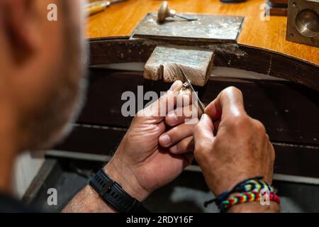 Homme joaillier Goldsmith travaillant dans son atelier de fabrication de bijoux créant et chaulant un bijou en or blanc ou en argent dans son atelier de travail. Banque D'Images