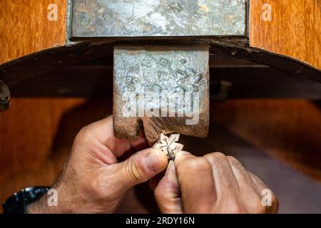 Homme joaillier Goldsmith travaillant dans son atelier de fabrication de bijoux créant et réparant un bijou en or blanc ou en argent avec un burin dans son atelier de travail. Banque D'Images