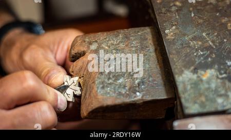 Homme joaillier Goldsmith travaillant dans son atelier de fabrication de bijoux créant et réparant un bijou en or blanc ou en argent avec un burin dans son atelier de travail. Banque D'Images