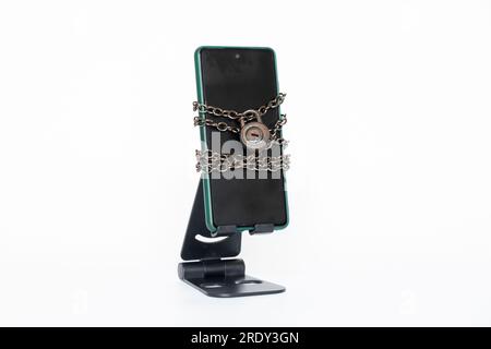 Téléphone portable sur une chaîne avec une serrure sur un support sur un fond blanc, protection et sécurité du téléphone Banque D'Images