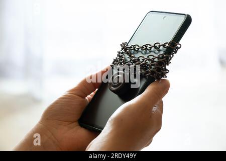 Téléphone portable attaché avec sur un cadenas de chaîne dans les mains d'une fille, protection en sécurité du téléphone Banque D'Images