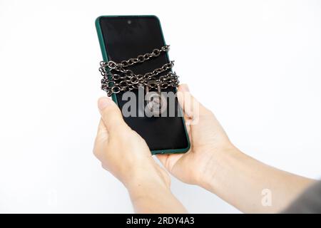 Téléphone portable attaché avec sur un cadenas de chaîne dans les mains d'une fille, protection en sécurité du téléphone Banque D'Images