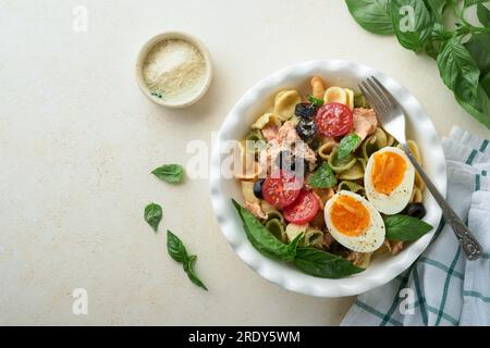 Salade de pâtes italiennes. Pâtes orecchiette au thon, à la tomate cerise, à l'olive, au basilic et au parmesan dans une assiette sur fond de pierre grise ou de béton. TRADI Banque D'Images