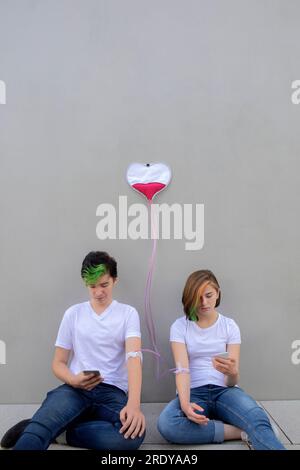 Couple d'adolescents connecté avec des gouttes IV en utilisant des téléphones intelligents près du mur de béton Banque D'Images