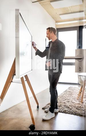 Homme d'affaires avec écriture au stylo numérisé sur tableau blanc interactif vu à travers le verre Banque D'Images