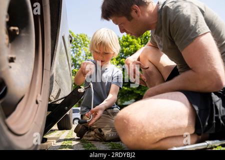 Père et fils changeant le pneu de voiture dans la cour Banque D'Images