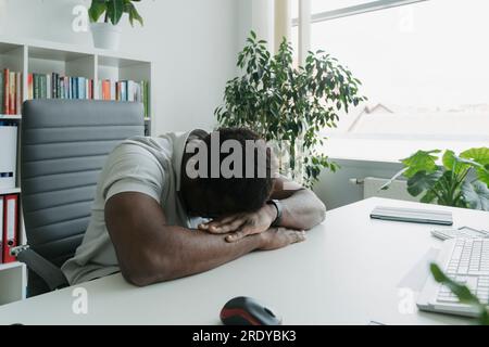 Homme d'affaires se reposant avec le visage vers le bas sur le bureau dans le bureau Banque D'Images