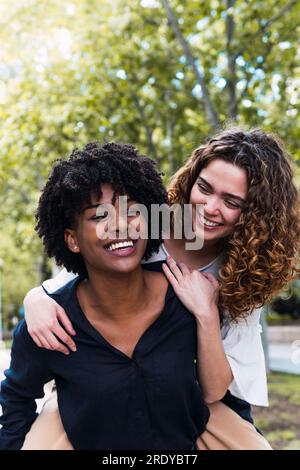 Heureuse jeune femme donnant tour de piggyback à un ami dans le parc Banque D'Images