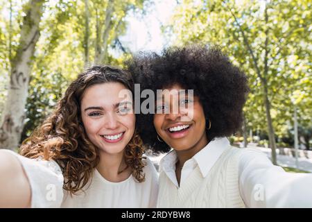 Heureux amis multiraciaux prenant selfie ensemble dans le parc Banque D'Images