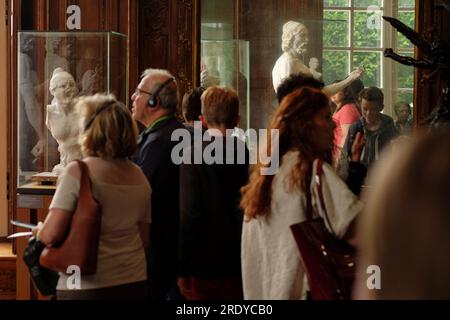 Les personnes portant des écouteurs font une visite audioguidée des galeries d'art lambrissées du Musée Rodin avec de grands miroirs, des fenêtres hautes, des sculptures et des peintures Banque D'Images