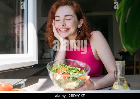 Femme heureuse avec bol de salade appuyé sur le comptoir de cuisine Banque D'Images